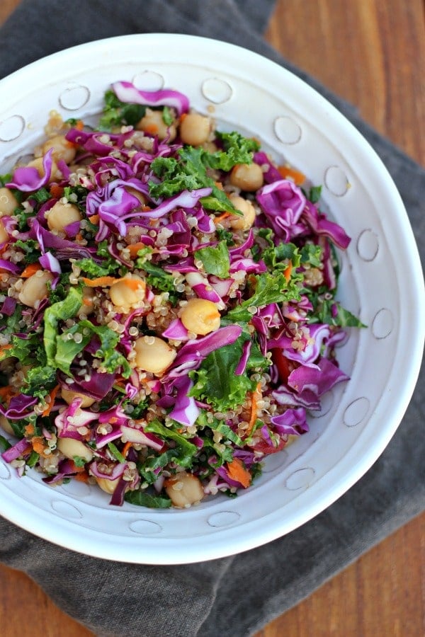 Quinoa, chickpeas, cabbage and kale salad in a round white bowl. A grey towel under the bowl on a wooden table. 