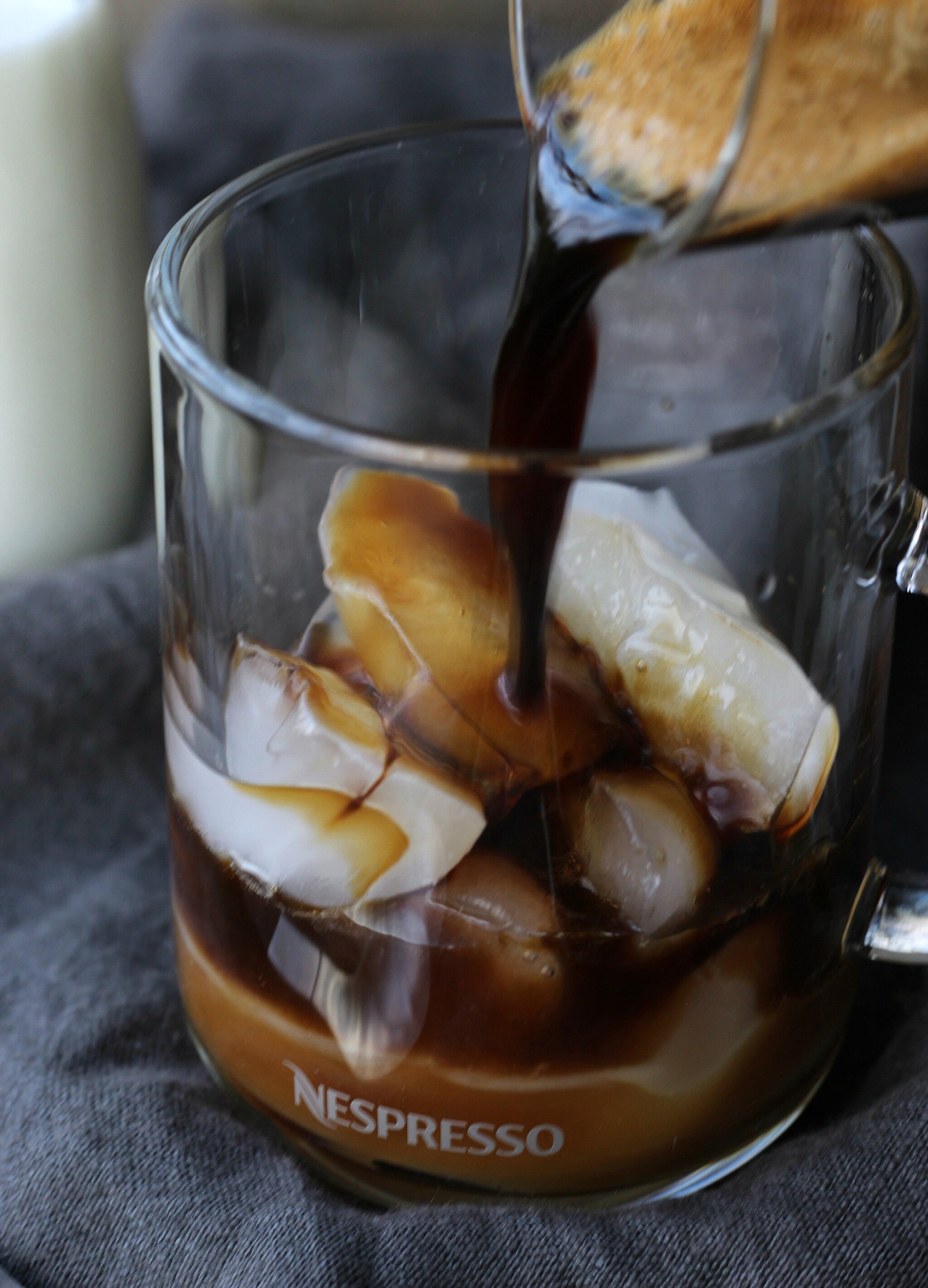 Espresso poured in a clear glass cup of caramel and ice cubes