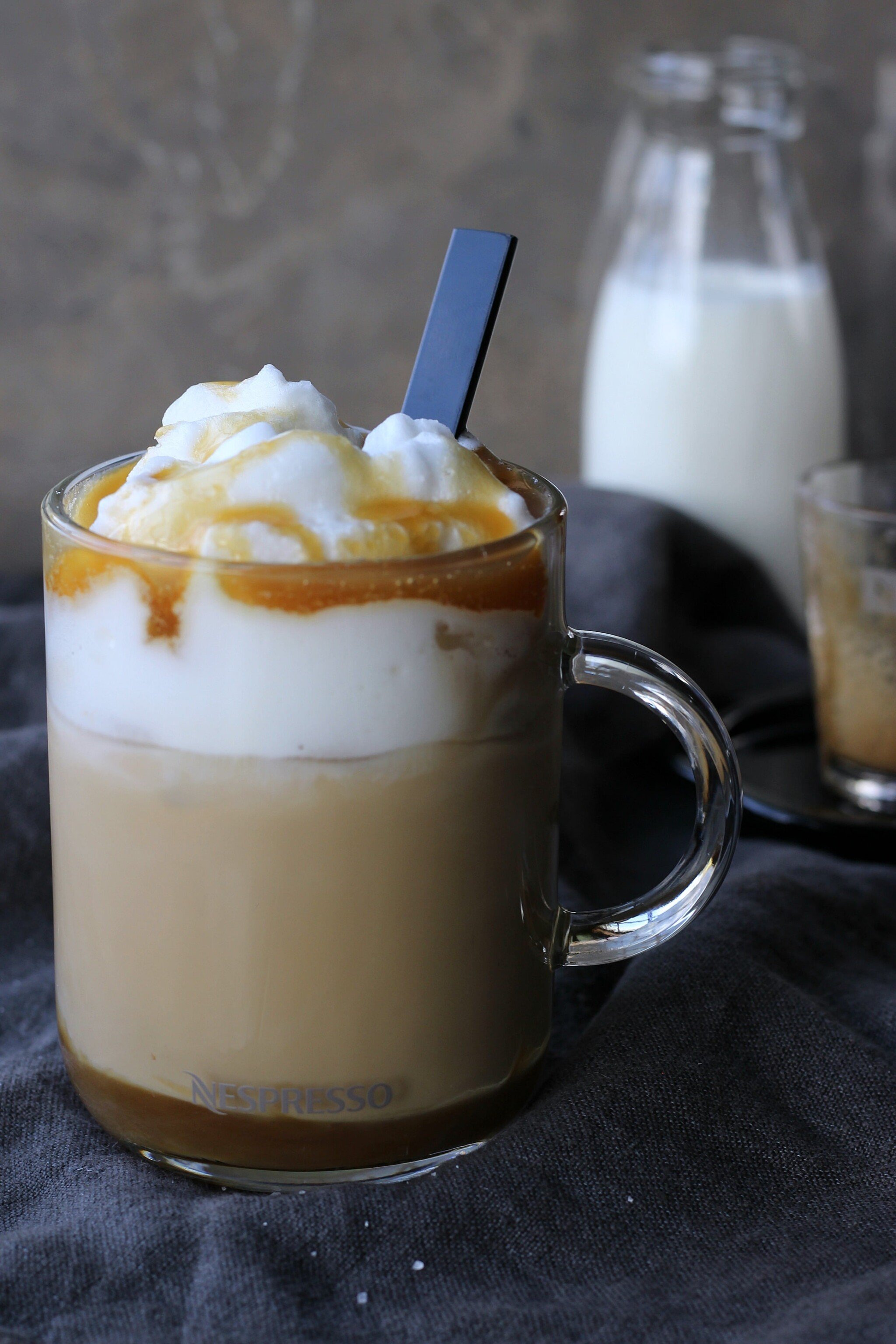 A clear glass cup with layers of an iced caramel macchiato with a stirrer