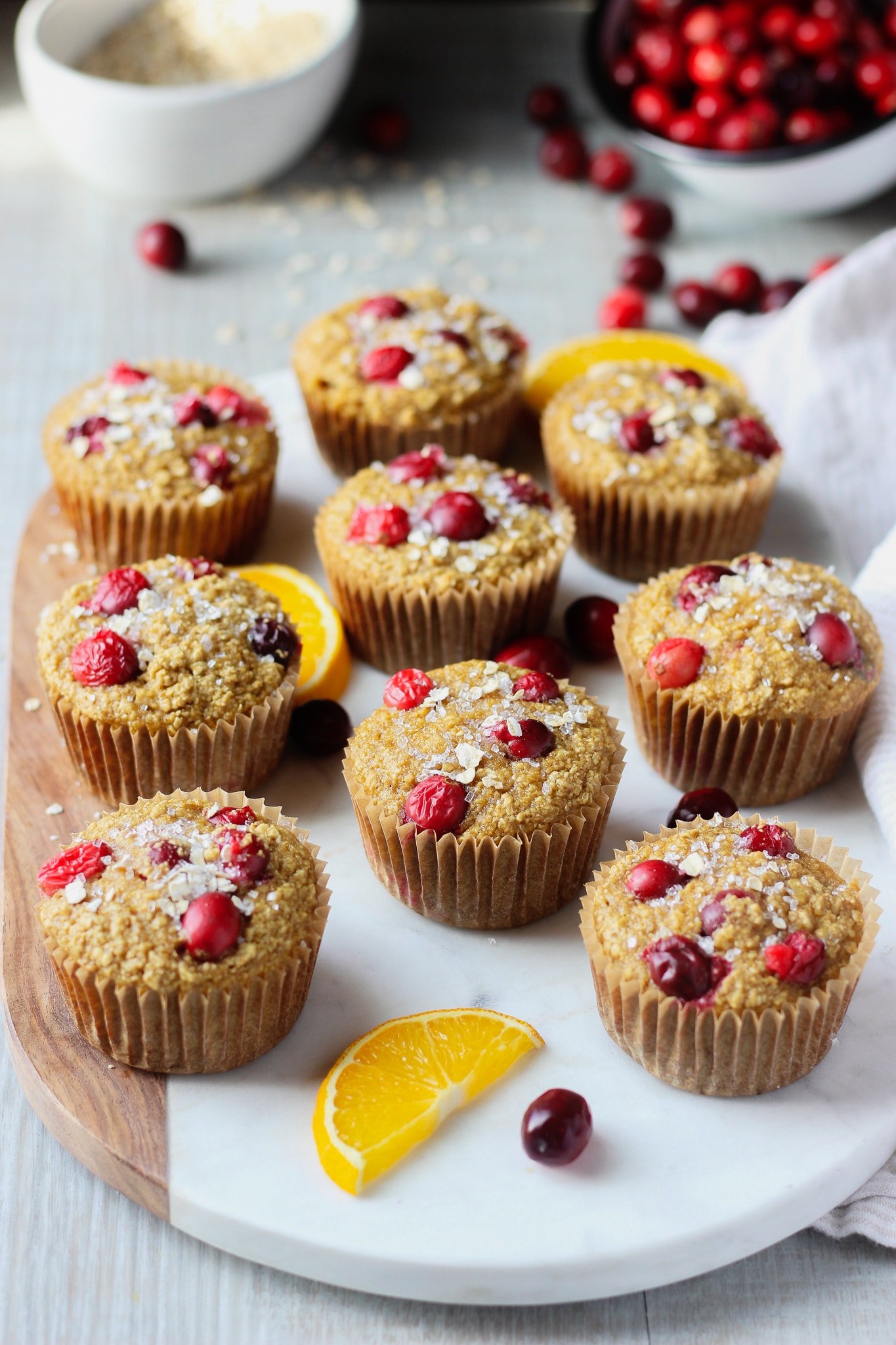 Cranberry Orange Muffins on a chopping board with orange slices and fresh cranberries surrounding it