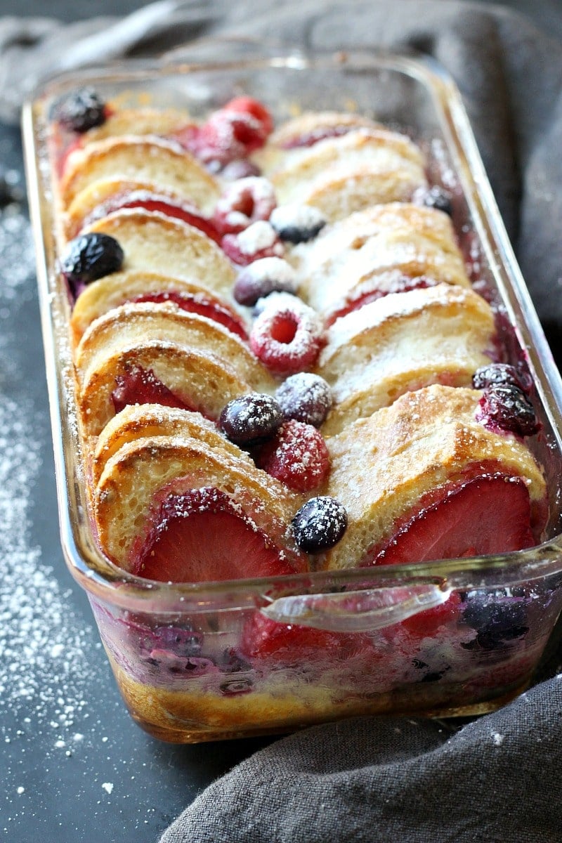 Sliced berry French toast, blueberries, raspberries, strawberries, icing sugar in a glass dish.