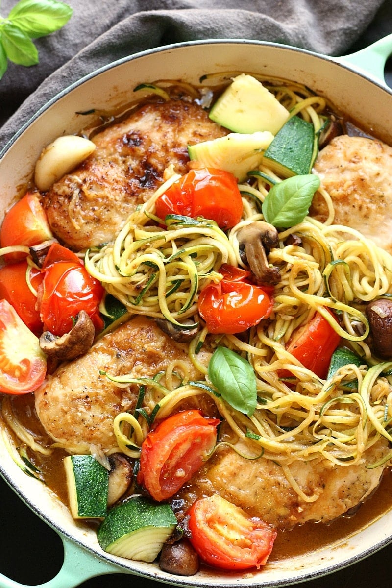 Healthy Low-Carb Chicken Zoodle Skillet with chicken, zucchini, tomatoes, mushrooms, fresh basil over zucchini noodles in a white ceramic pan with mint colored handles and a grey napkin.