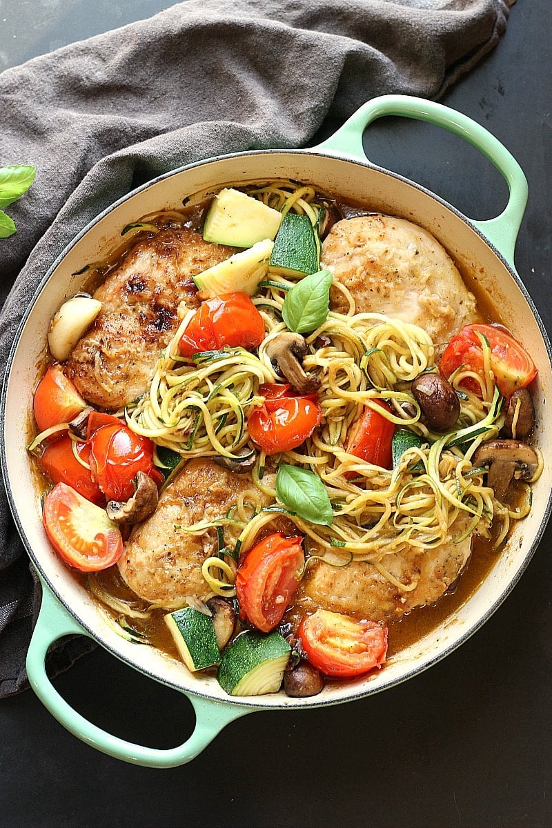 Healthy Low-Carb Chicken Zucchini Skillet with chicken, mushrooms, tomatoes, zucchini, fresh basil over zucchini noodles in a white ceramic pot with mint colored handles and a grey napkin.