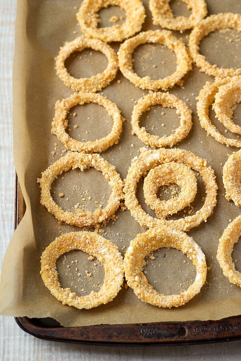 breaded onion rings on a parchment-lined baking sheet.