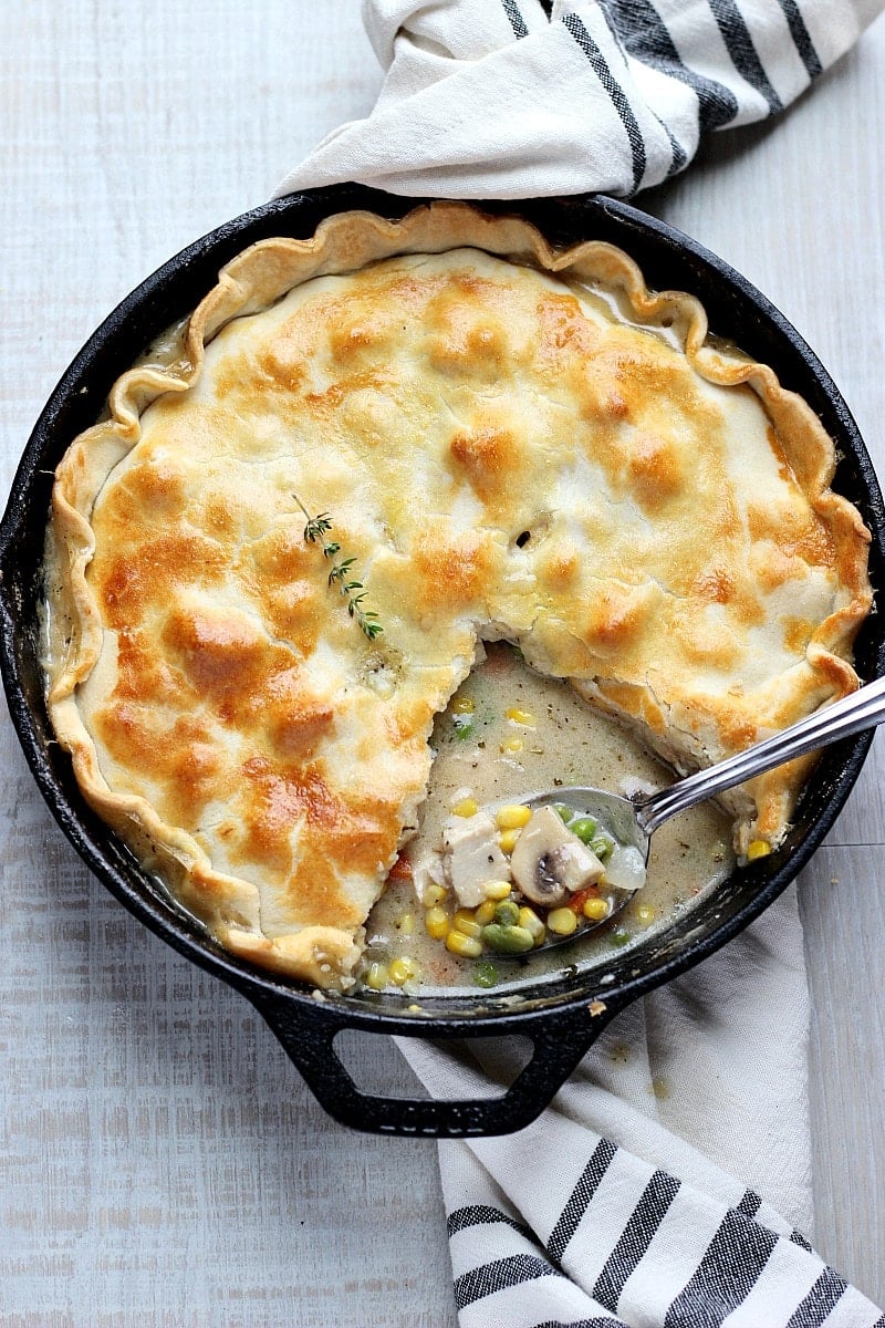 Skillet chicken pot pie in a black cast iron pan with a spoon and black and white dish towel. 
