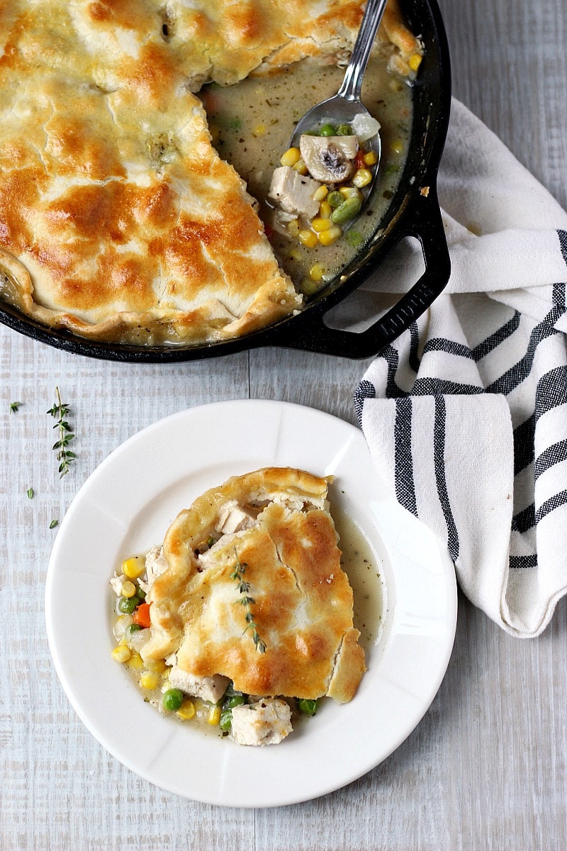 Skillet Chicken Pot Pie in a black cast iron skillet with a spoon and white and black dish towel and chicken pot pie on a white plate. 