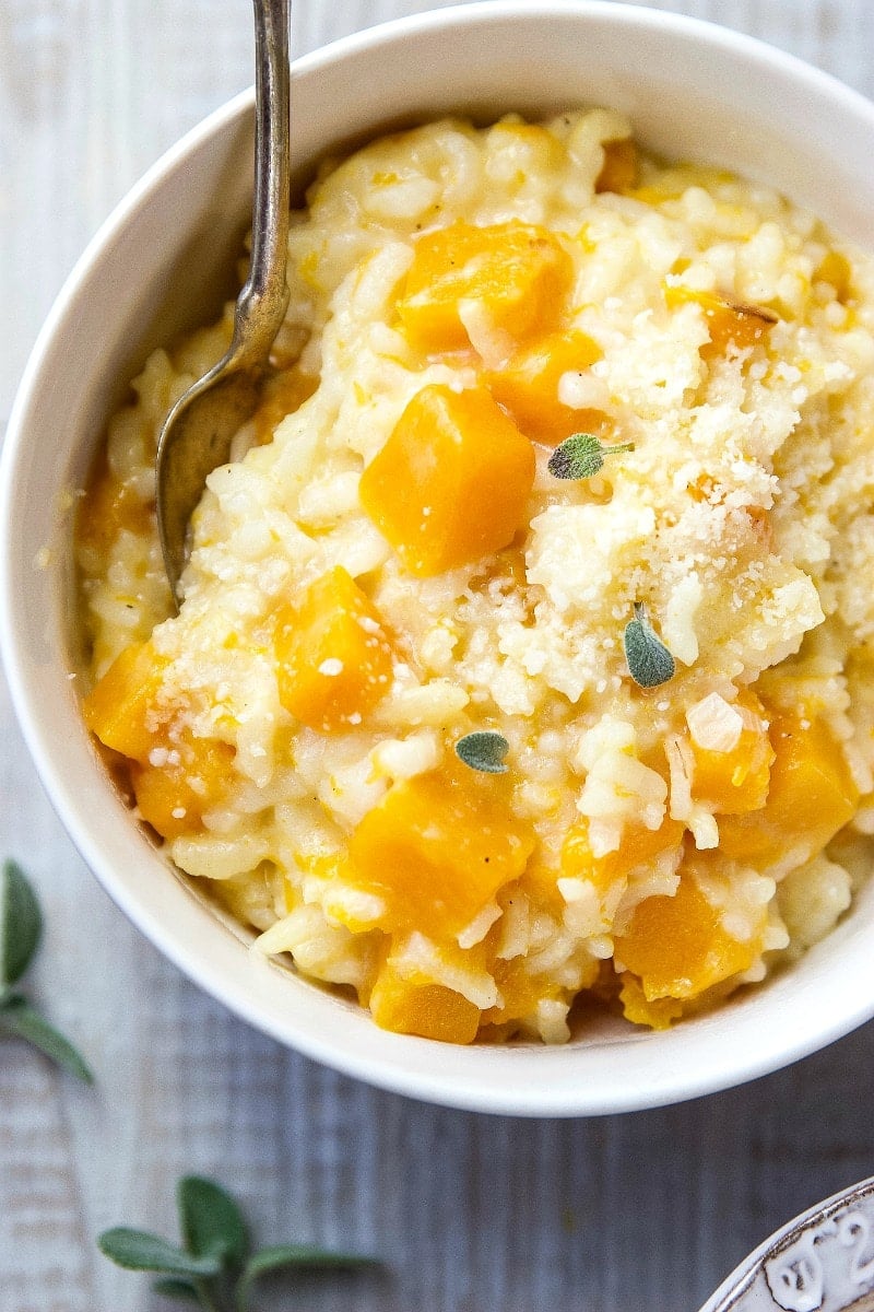 Butternut Squash Risotto topped with fresh sage in a small white bowl with spoon