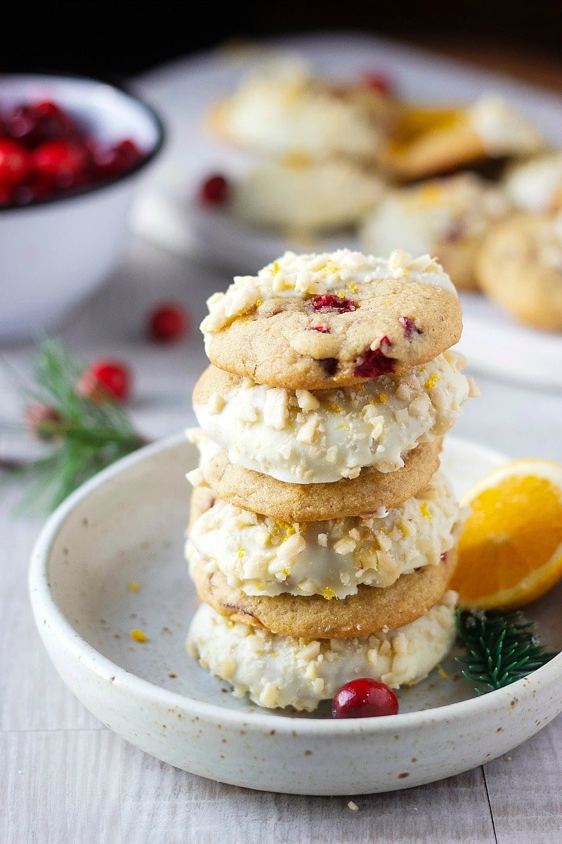 Cookies stacked on a small round plate and half dipped in white chocolate, cranberries, orange slice
