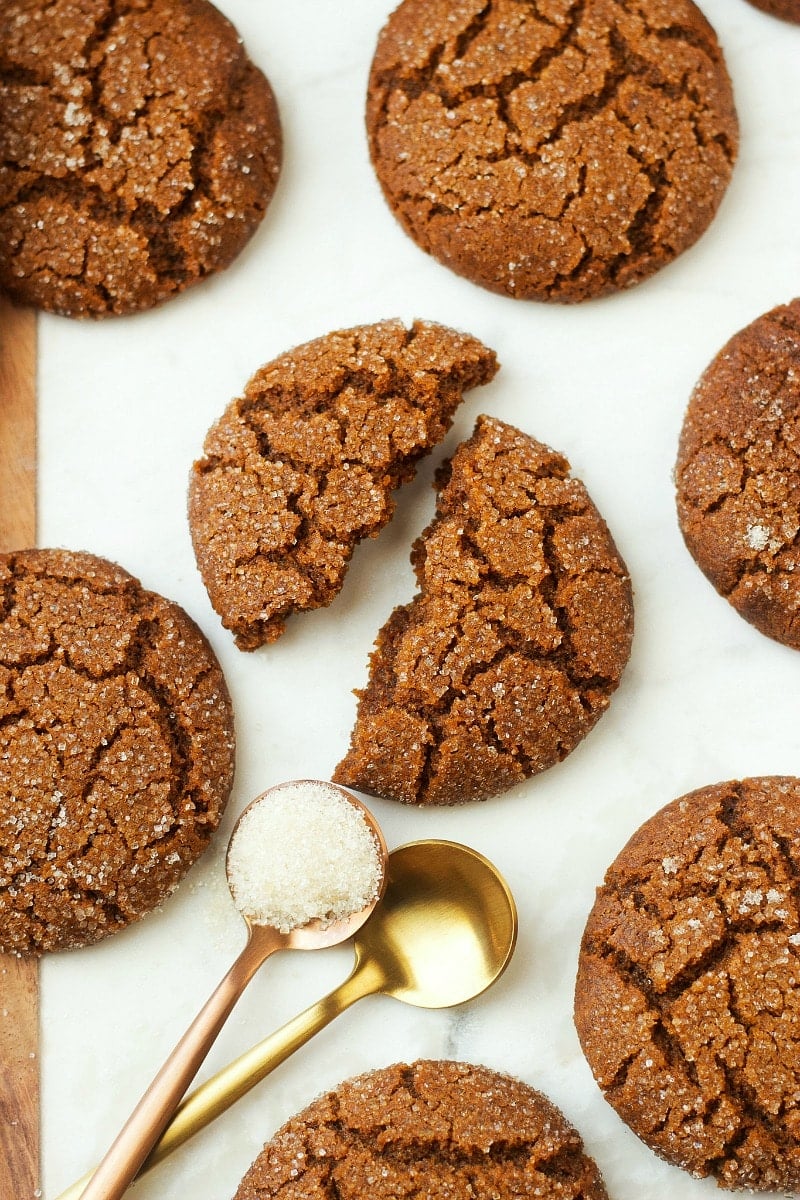 Soft cookies with one piece halved surrounded by a couple of gold-colored teaspoons with sugar