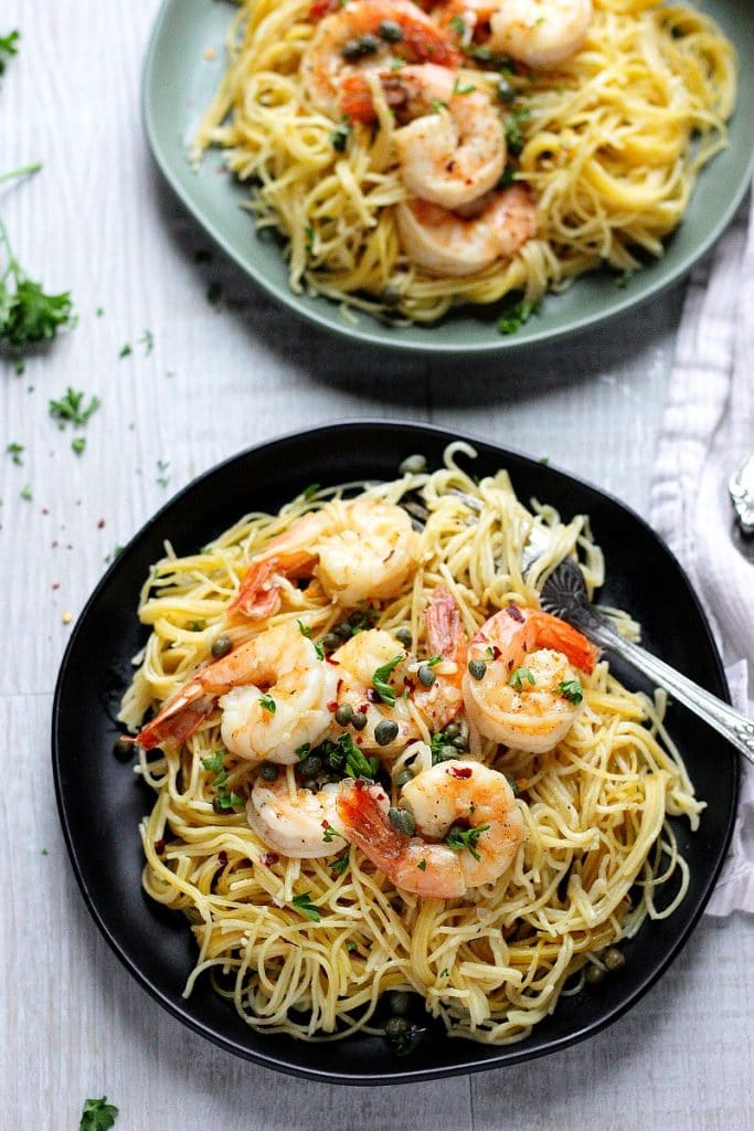 two plates serving Instant Pot Shrimp Scampi Pasta. Some herbs on the table.