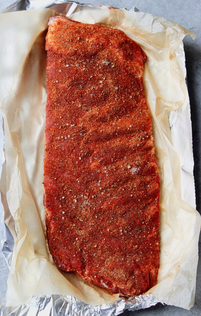 rack of spare ribs with dry rub seasoning on top on aluminum foil and a layer of parchment 