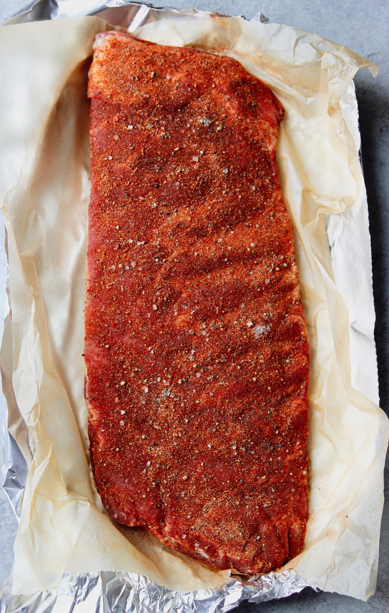 rack of spare ribs with dry rub seasoning on top on aluminum foil and a layer of parchment.
