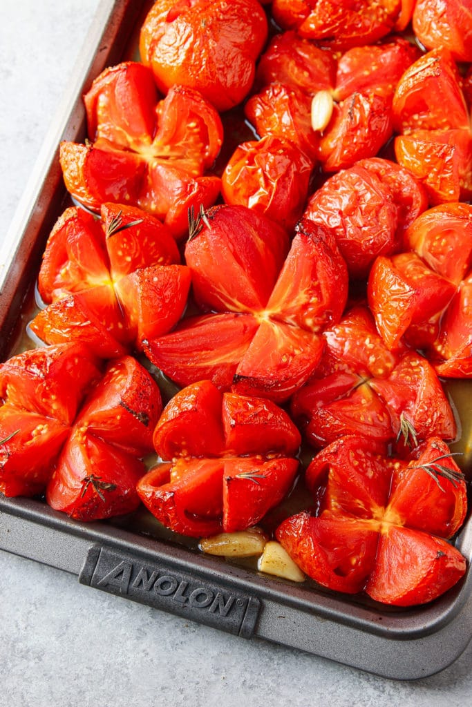 Quarter slices of fresh tomatoes on a sheet pan with garlic cloves.