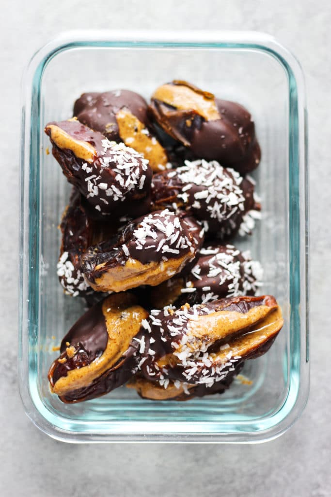 A rectangular glass container with chocolate-covered dates sprinkled with coconut flakes
