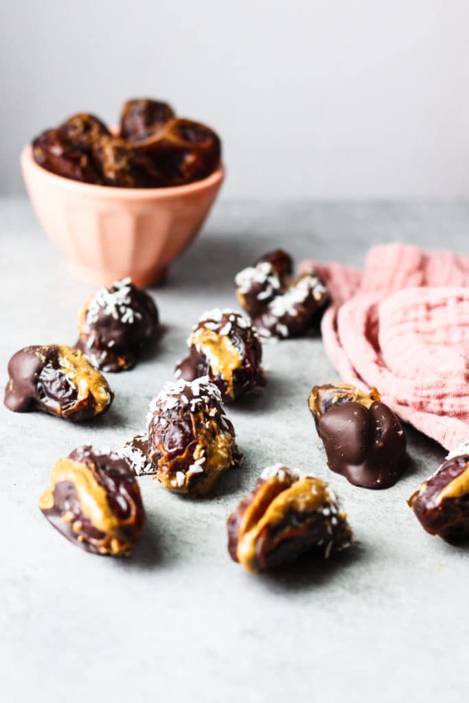 Dates stuffed with almond butter and covered with chocolate and a bowl of plain dates in the background