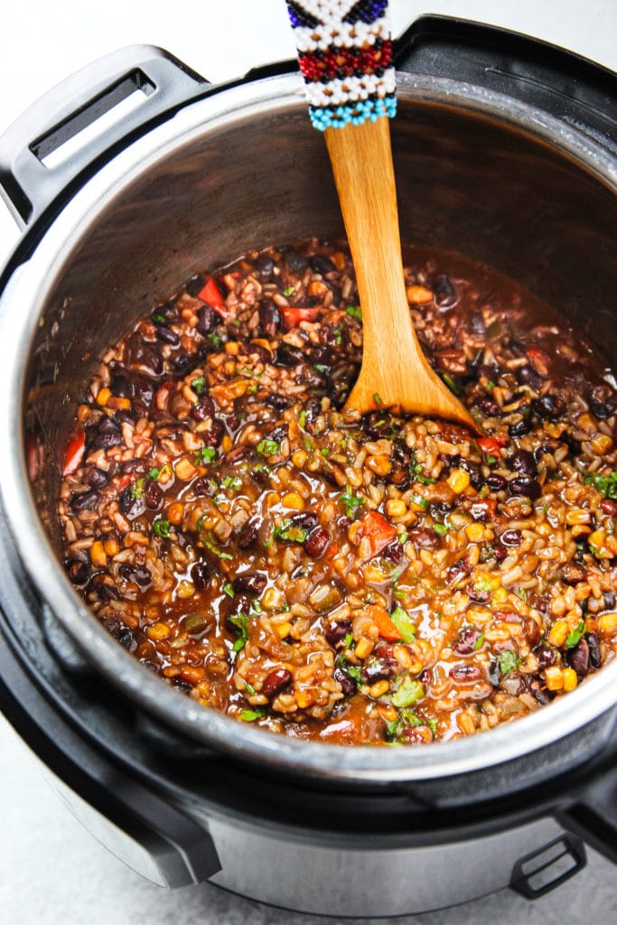 Ingredients of the Mexican beans and rice in an instant pot with a wooden spoon