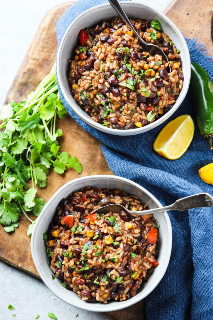 Two white bowls with a spoon on a wooden chopping board containing Mexican beans and rice