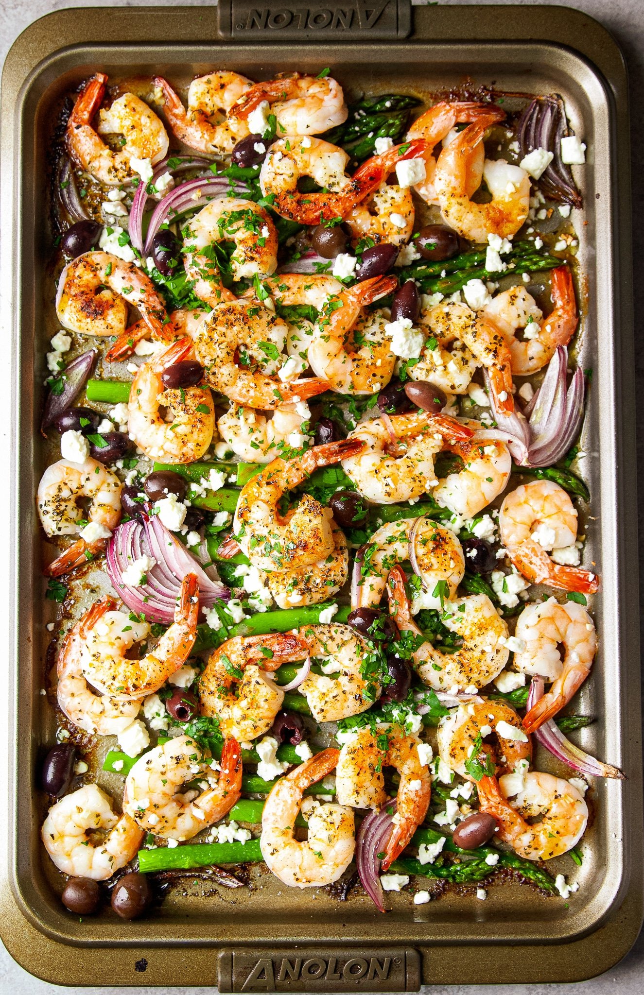 Cooked shrimp, onions, and asparagus mixed with seasonings and feta cheese on a sheet pan