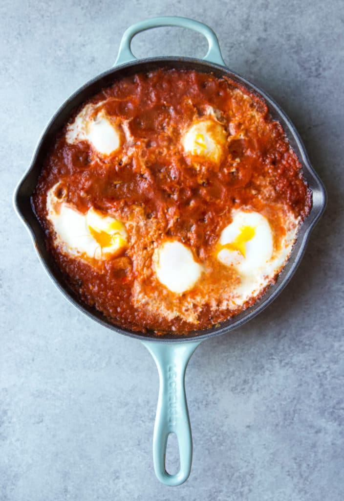 Poached eggs in a tomato-based mixture in a cast iron skillet without the toppings