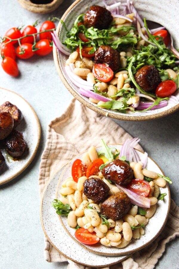 White Bean Salad topped with chicken meatballs in a shallow bowl and a small plate, a few cherry tomatoes and a small plate of chicken meatballs.