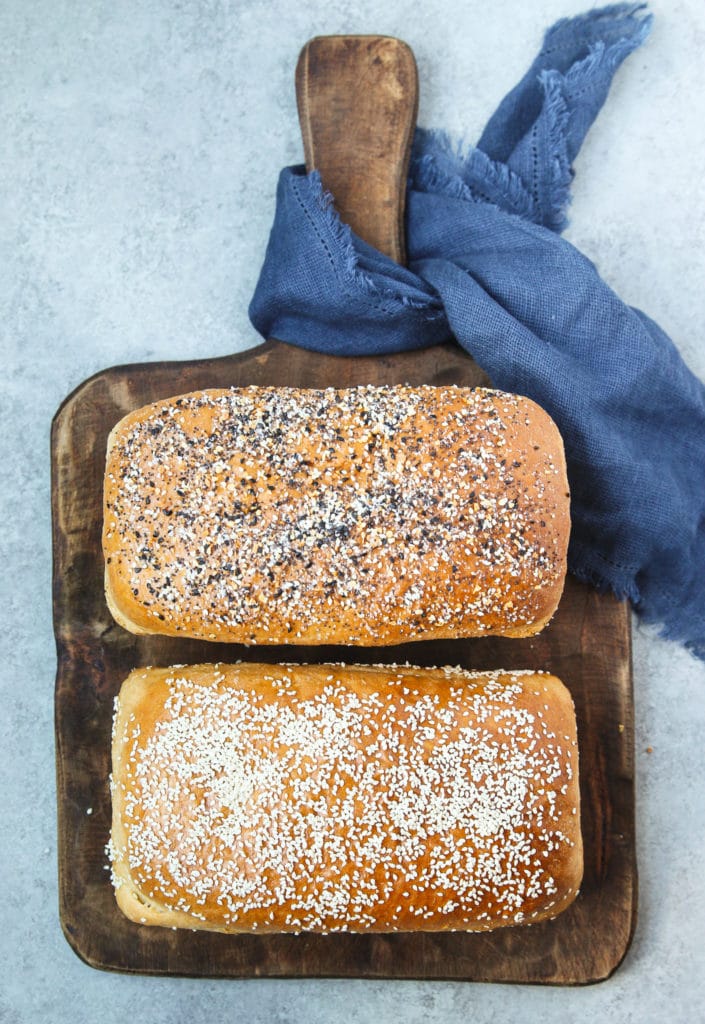Two loaves of bread on a chopping board  with sesame seeds toppings.