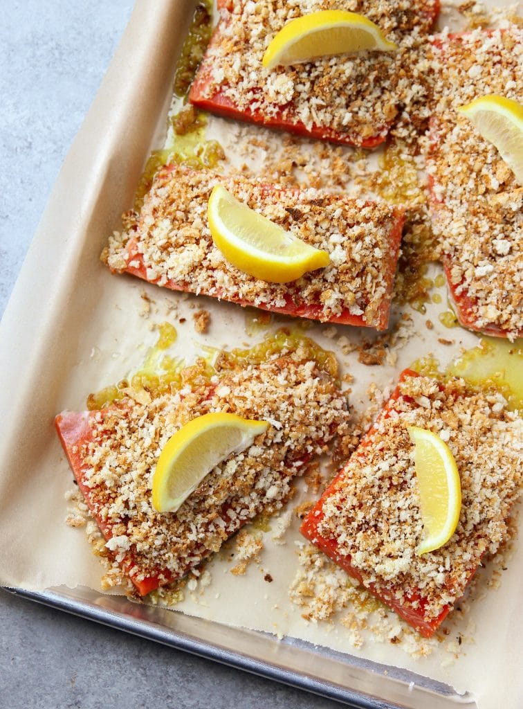 Crispy onion Parmesan salmon with slices of lemon on a tray lined with parchment paper