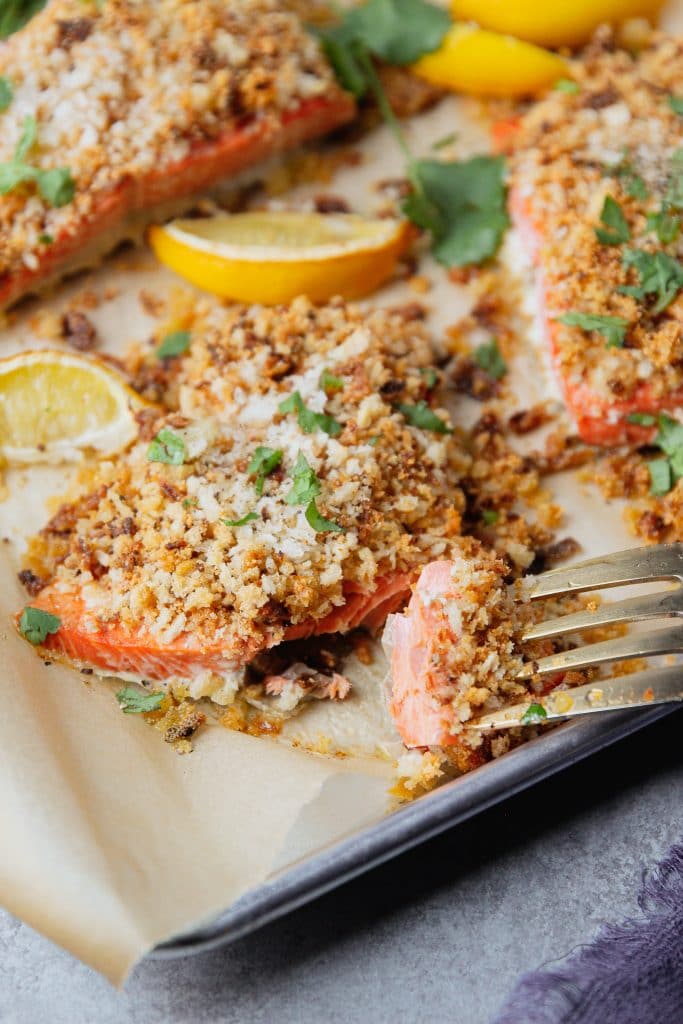 Crispy onion Parmesan salmon on a tray with a bite-size of a slice of it on a fork