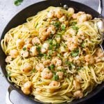 Shrimp scampi pasta in a skillet with two handles topped with shrimp, fresh parsley, pepper flakes, and grated Parmesan cheese