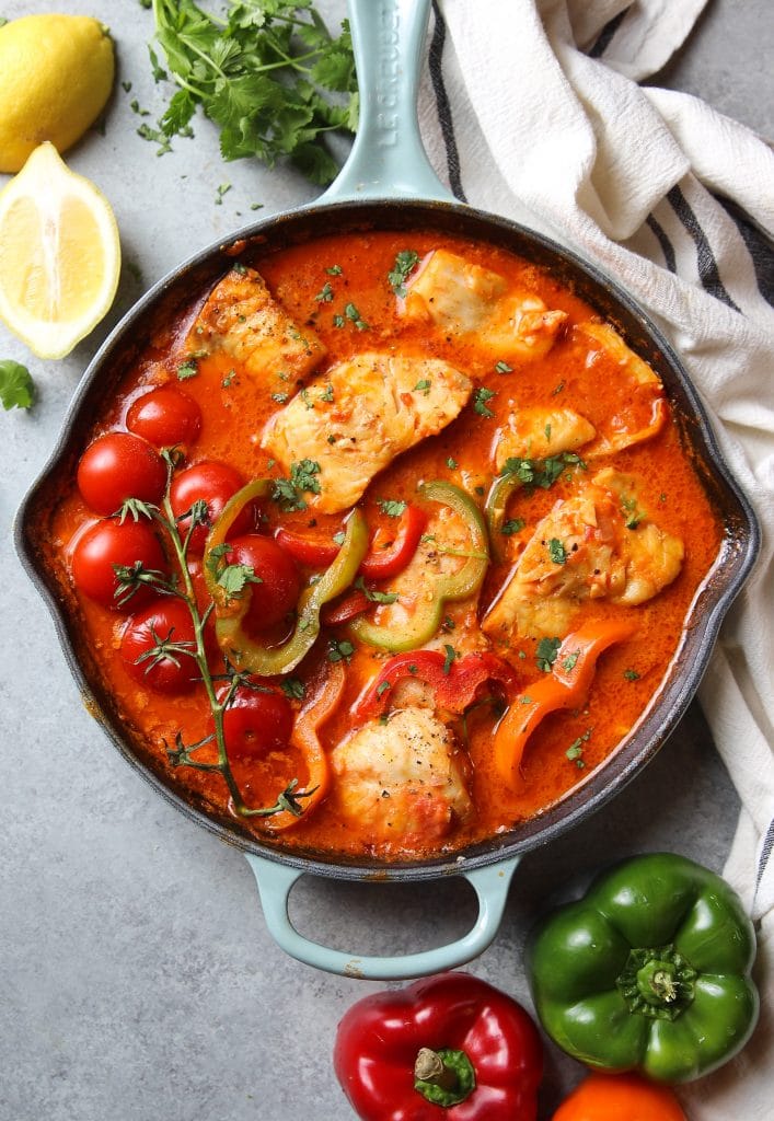 fish stew (moqueca) with cod in a broth of tomato sauce, garnished with fresh cilantro, served in a cast iron skillet