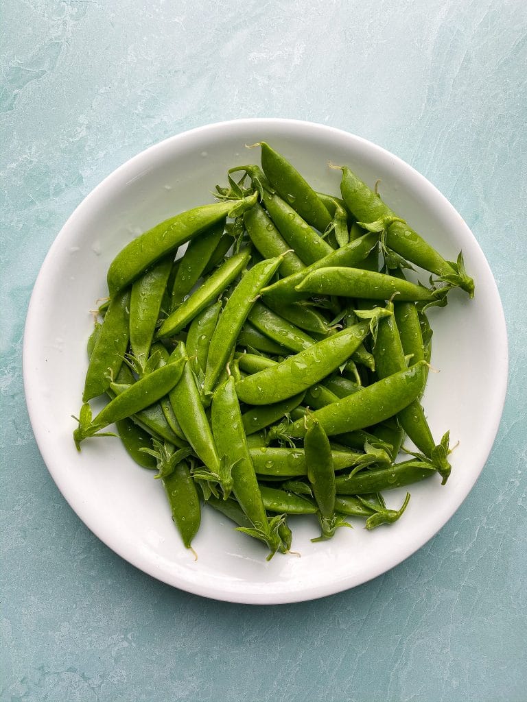 Freshly picked and washed snap peas  on a white round plate, on a blue board