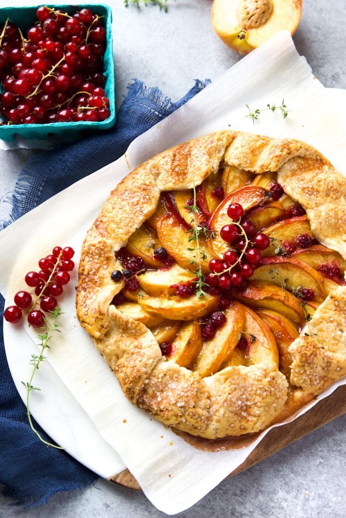 Rustic peach galette with homemade buttery crust, juicy peaches and fresh currants, sitting on parchment paper