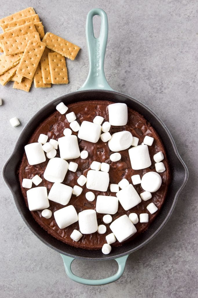 brownie s'mores dip in a blue cast iron skillet served with graham crackers and marshmallows