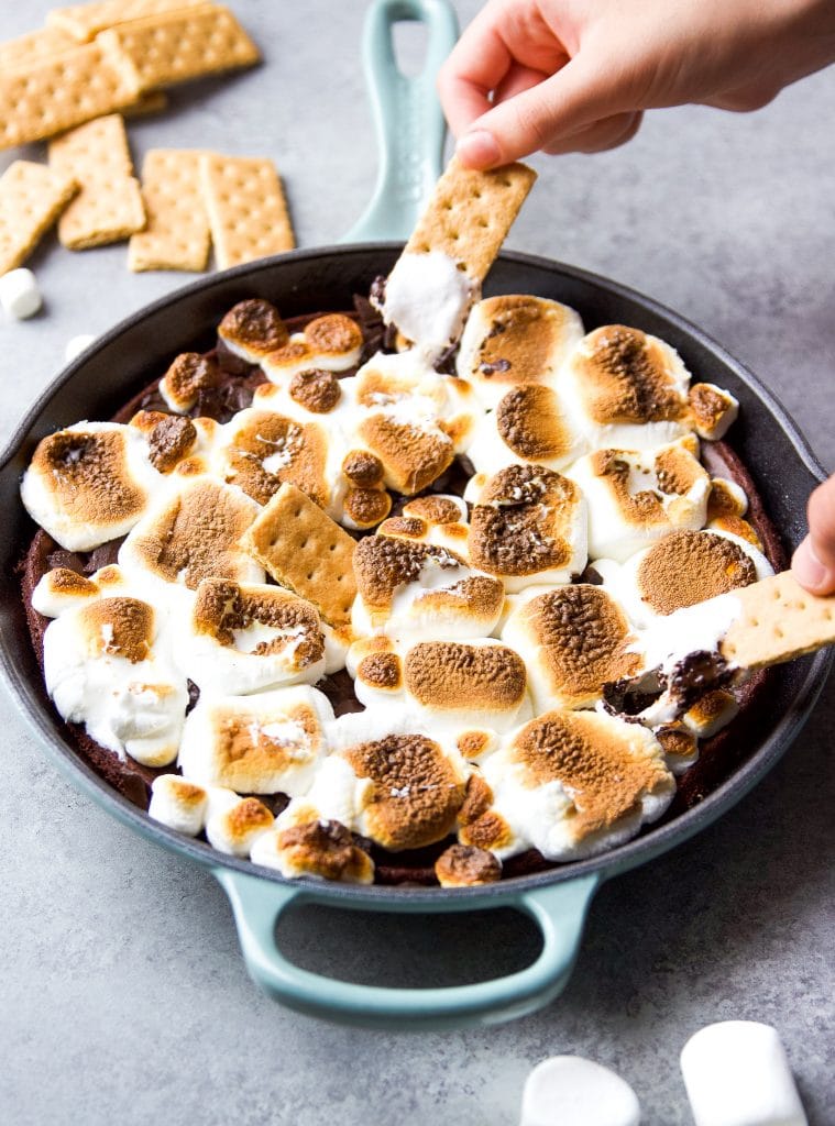 brownie s'mores dip in a blue cast iron skillet served with graham crackers and marshmallows. 