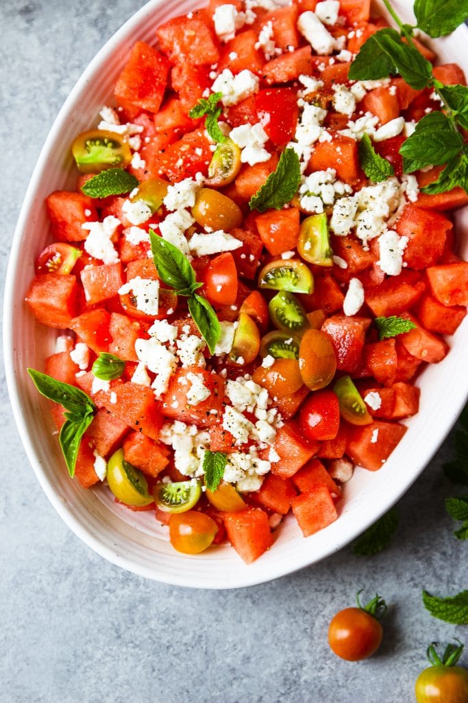 watermelon feta salad with fresh mint, basil and garden tomatoes serve in a large white oval bowl