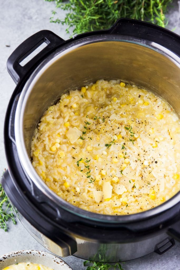corn risotto inside the instant pot. Risotto is topped with grated parmesan cheese and fresh thyme.