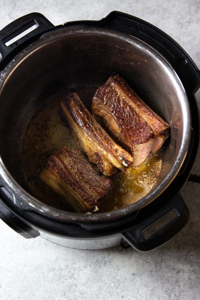 Beef short ribs being browned in an instant pot. 