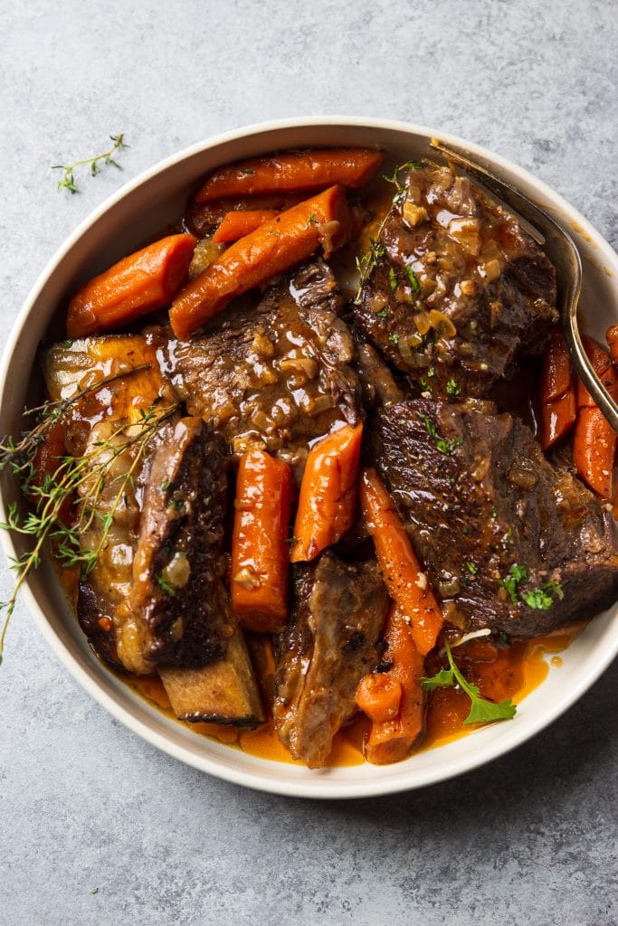 A plate of short ribs with carrots and fresh thyme.