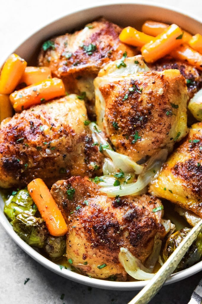 chicken thighs with vegetables in a round serving plate with fork and spoon