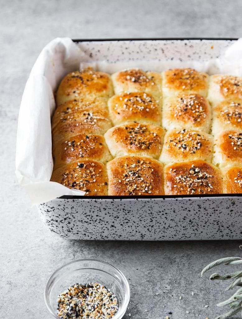 Dinner rolls freshly baked in baking dish. A small bowl with seasoning and dried herbs on the table