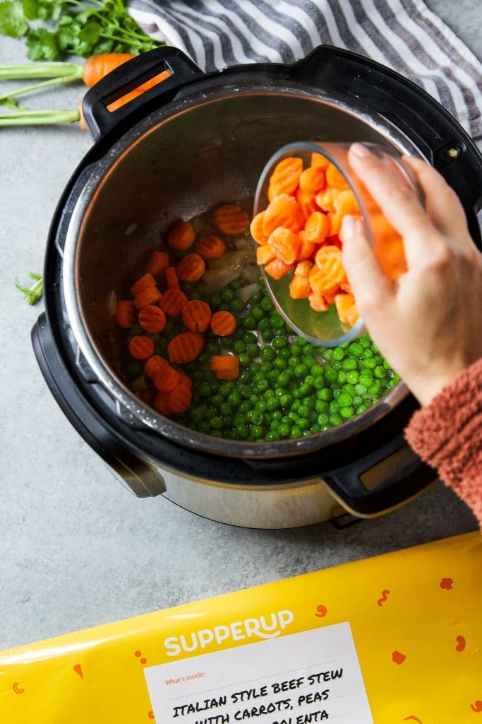Sliced carrots and fresh peas being added to the instant pot.