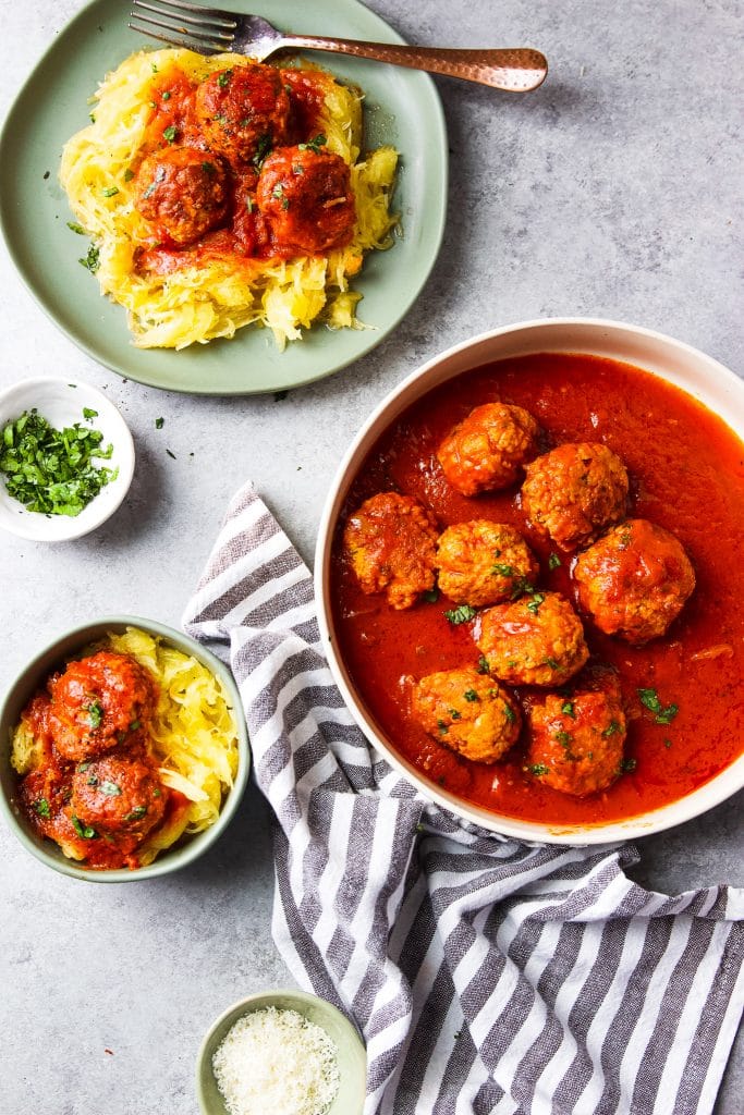 turkey meatballs and spaghetti squash on a plate with a fork. A plate with turkey meatballs in marinara sauce. a small bowl with fresh herbs
