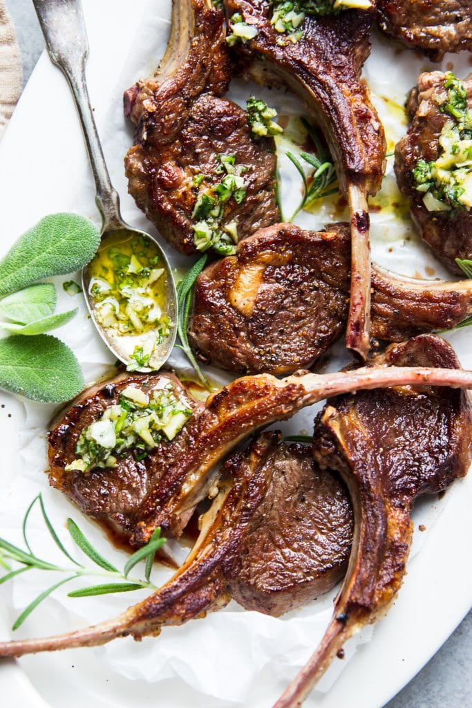 lamb chops served on a white platter with herb sauce