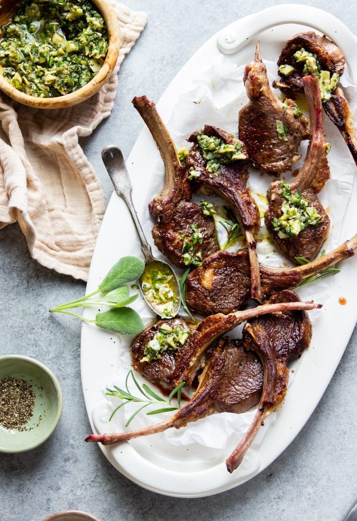 lamb chops served on a white platter with herb sauce