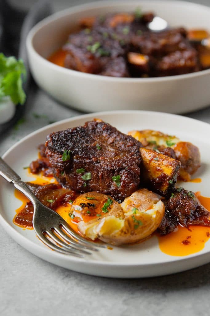 A plate with balsamic braised short ribs in oven with a smashed potatoes and a fork.