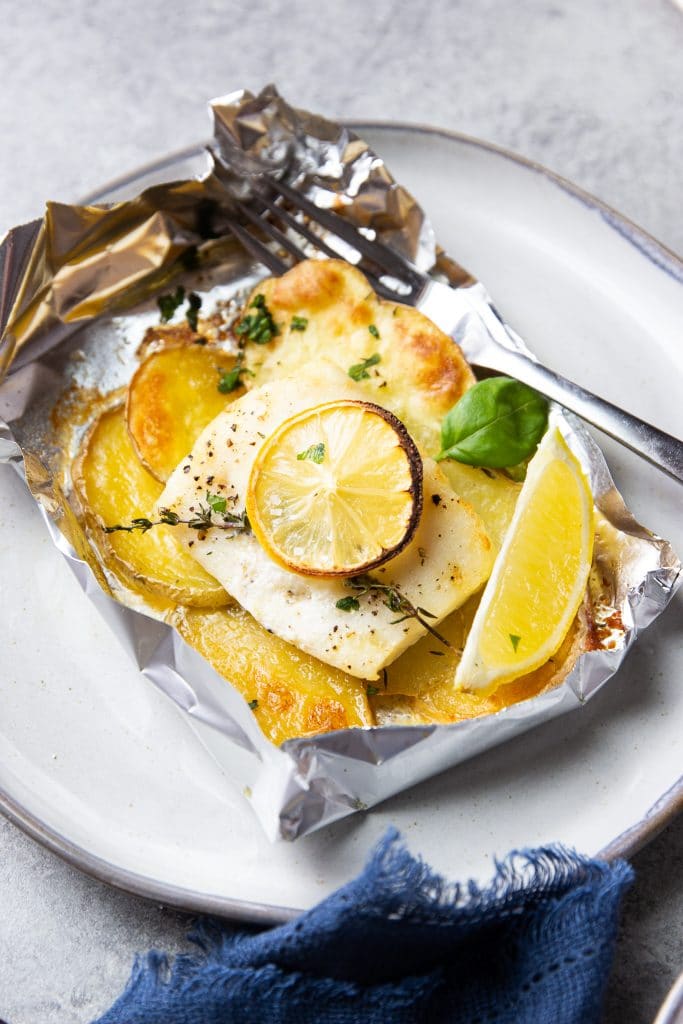 fish and potatoes baked in foil. A fish in foil packet on a plate with a fork