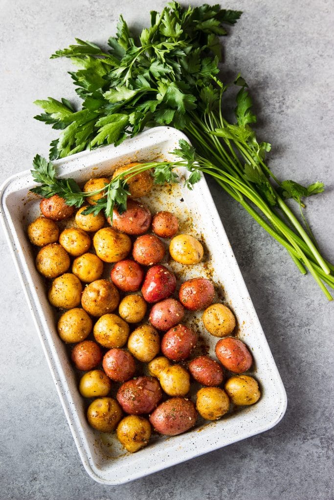 Seasoned baby potatoes in a white baking dish with parsley. 