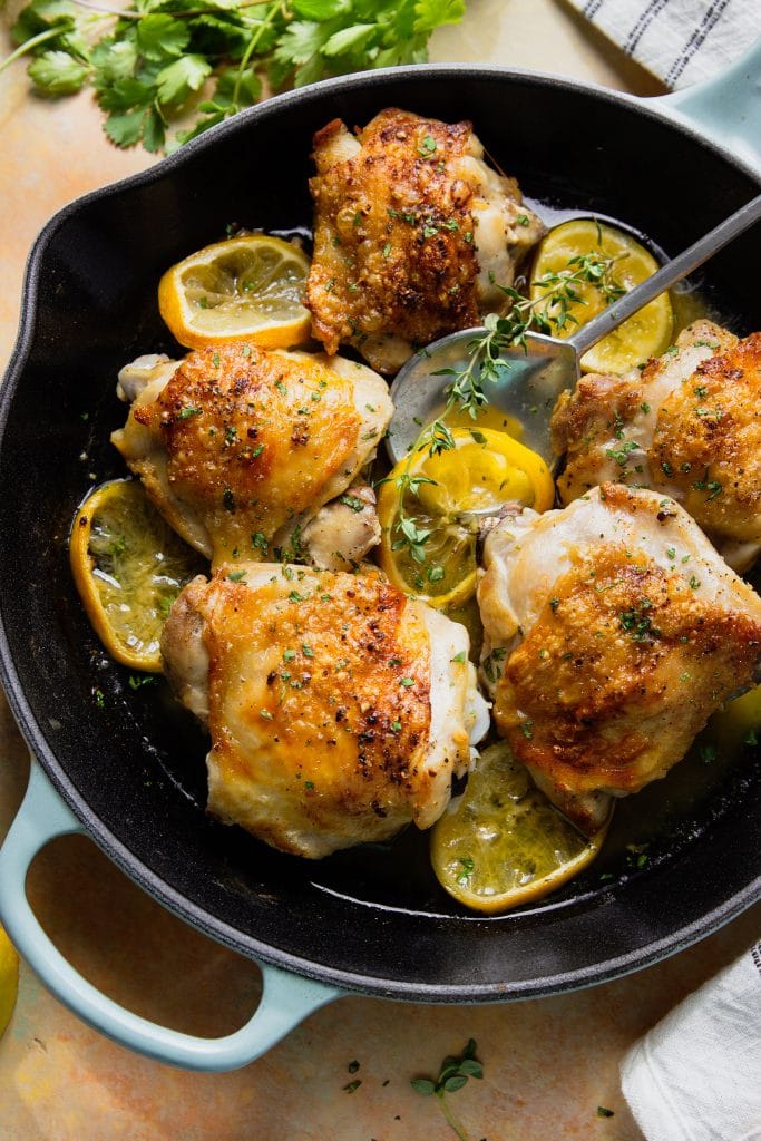 Butter chicken thighs in skillet with lemon slices and herbs