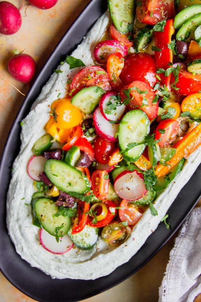 whipped feta dip on a platter topped with fresh veggies. 
