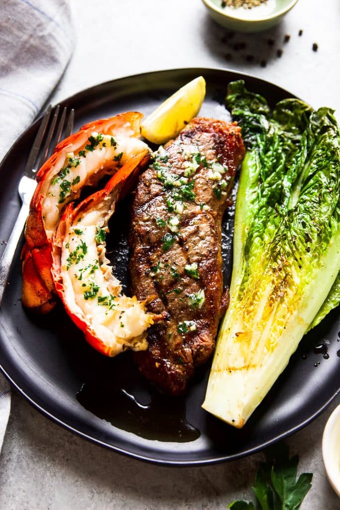 A plate with a grilled steak and lobster, grilled lettuce and a fork.