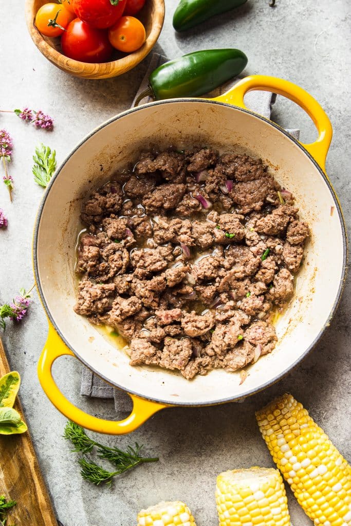 cooked ground beef in yellow skillet. Fresh herbs and ingredients on the table 